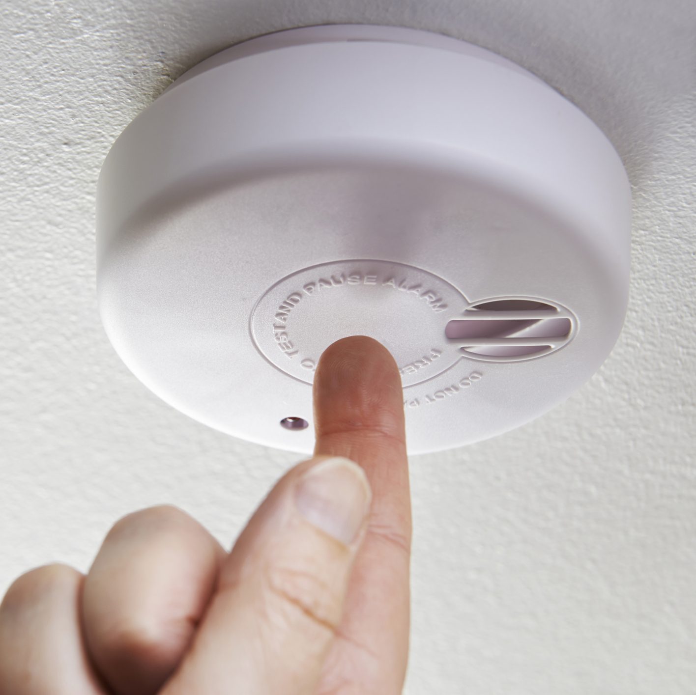 Close Up Of Hand Testing Domestic Smoke Alarm