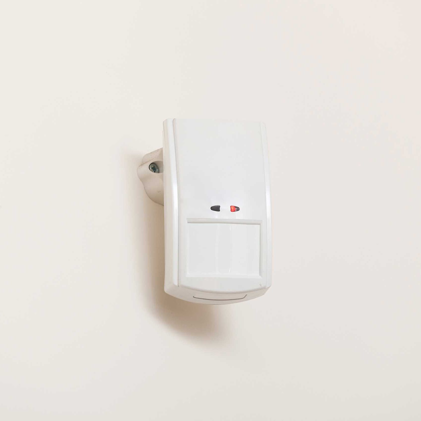 Motion sensor with light detector mounted on exterior wall of private house as part of security system.
